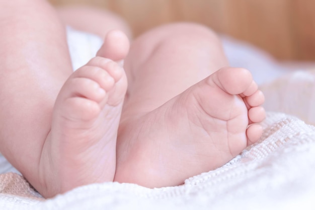 白い毛布の上の小さな赤ちゃんの足。ソフトベッドで寝ている乳児の小さな裸足のクローズアップ。ニット毛布に対してかわいい新生児。子供時代。眠っている新生児。
