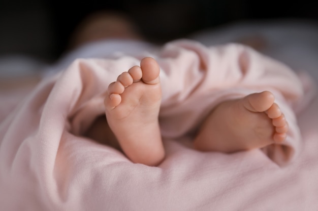 Tiny baby girl feet covered with soft pastel peach blanket, adorable small toes