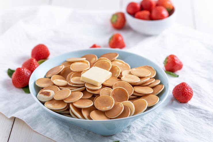 Tiny cereal pancakes in blue plate with strawberries on white