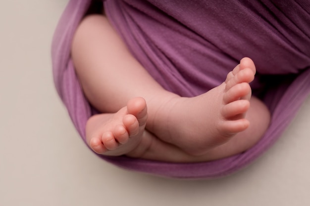 Крошечные, милые, босые ножки маленькой кавказской новорожденной девочки-мальчика, завернутые в сиреневое мягкое и уютное одеяло .. Фото высокого качества
