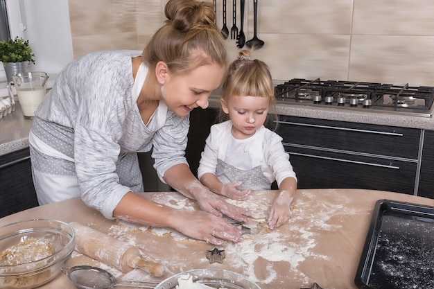 A tiny daughter spends time with her mother in the kitchen to bake cookies