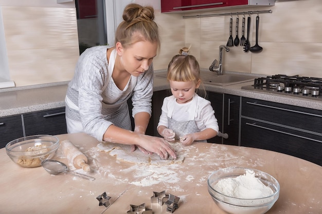 A tiny daughter spends time with her mother in the kitchen to bake cookies