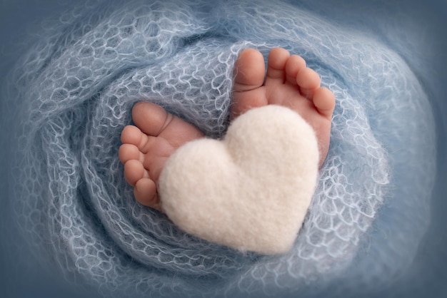 The tiny foot of a newborn baby Soft feet of a new born in a blue wool blanket Close up of toes heels and feet of a newborn Knitted white heart in the legs of a baby Macro photography