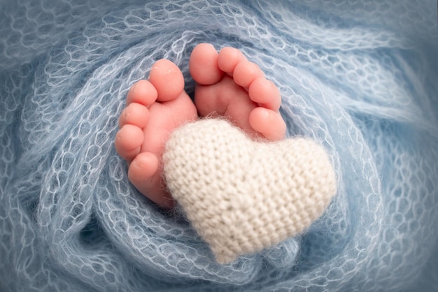 The tiny foot of a newborn baby Soft feet of a new born in a blue wool blanket Close up of toes heels and feet of a newborn Knitted white heart in the legs of a baby Macro photography