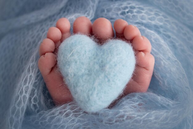 The tiny foot of a newborn baby Soft feet of a new born in a light blue blanket Close up of toes heels and feet of a newborn Knitted blue heart in the legs of a baby Studio macro photography