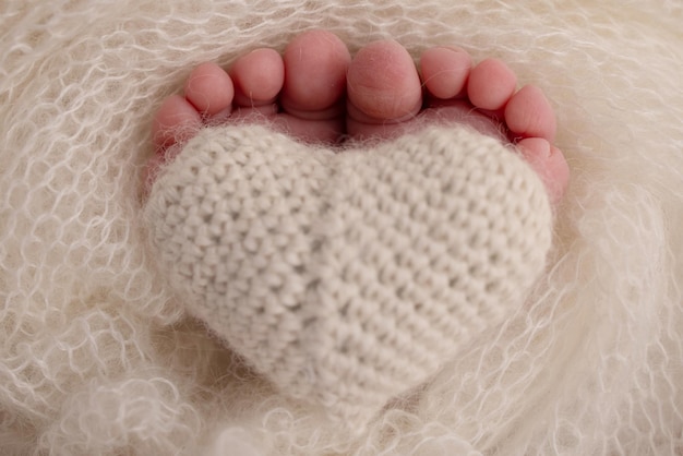 The tiny foot of a newborn baby Soft feet of a new born in a wool white blanket Closeup of toes heels and feet of a newborn Knitted heart in the legs of baby Macro studio photography