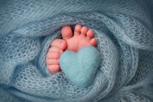 Tiny foot of a newborn Soft feet of a newborn in a turquoise woolen blanket Closeup the toes heels and feet of a newborn baby Knitted turquoise heart in the legs of a baby Macro photography