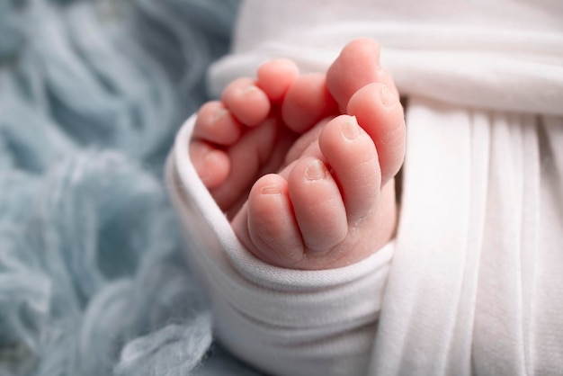 The tiny foot of a newborn Soft feet of a newborn in a white blanket and on a blue background Close up of toes heels and feet of a newborn baby Studio Macro photography Woman39s happiness