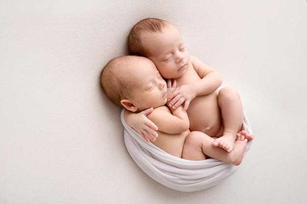 Tiny newborn twins boys in white cocoons on a white background A newborn twin sleeps next to his brother Newborn two twins boys hugging each otherProfessional studio photography