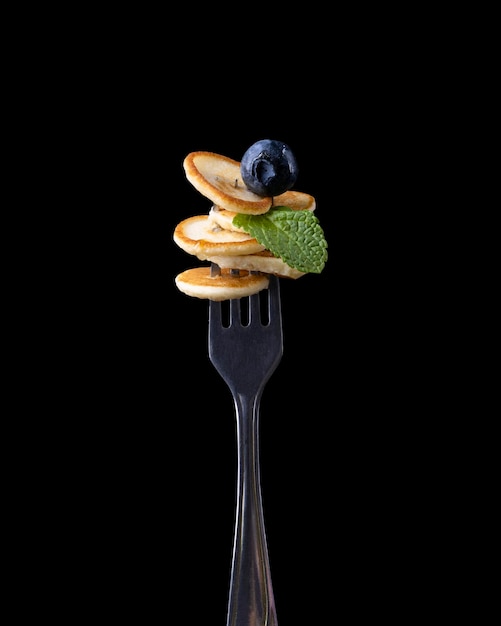 Tiny pancake with berries on a fork on a dark background.