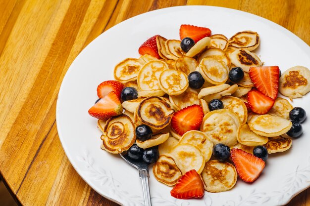 朝食に小さなパンケーキ。イチゴとブルーベリーのパンケーキは、家庭の台所で朝食をとるために午前中に調理されました。