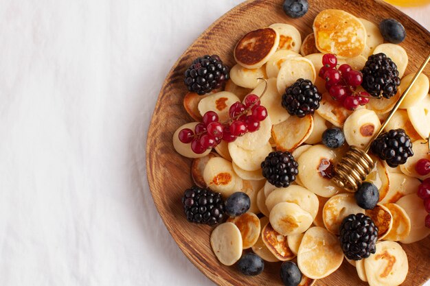 Piccole frittelle con frutti di bosco in primo piano su una tovaglia bianca. porridge di pancake. il concetto di tendenze della colazione nella fornitura.