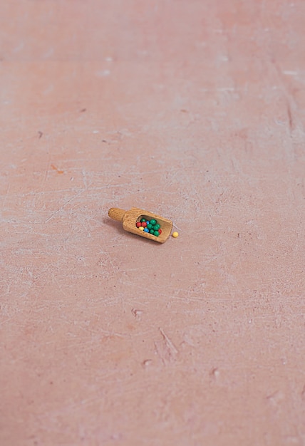 A tiny wooden scoop with colourful candy sprinkles on a pink aged concrete background. Minimal creative food flat lay.