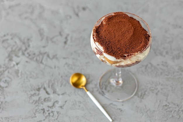 Tiramisu dessert in a glass on gray surface