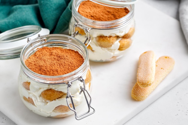 Tiramisu-dessert in potten met een deksel op een marmeren bord en een grijze achtergrond groene servet Tiramisu cake