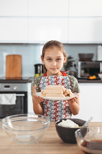 Tiramisu making process in the kitchen little girl making Italian desert with cocoa and espressodipped ladyfingers with mascarpone cream step by step 1