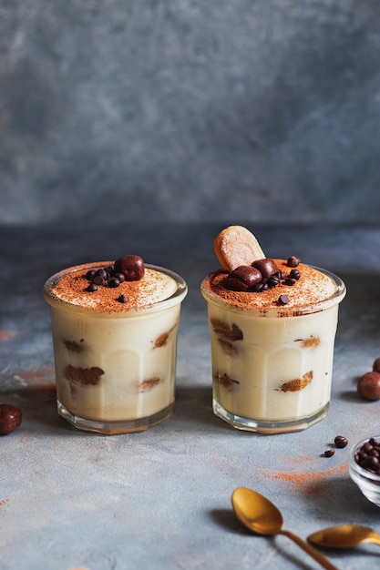 Tiramisù. dolce tradizionale italiano sul vetro su sfondo grigio pietra decorato con gocce di cioccolato cosparse di polvere di cocao