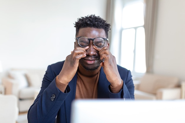 Tired African American businessman taking off glasses exhausted employee massaging nose bridge suffering from eye strain after long computer work feeling pain health problem concept