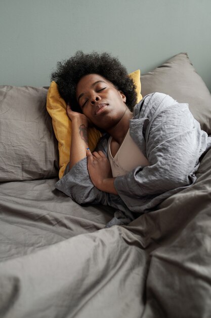 Tired african woman lying under blanket in bed