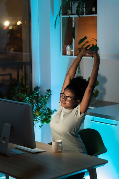 Tired african young woman takes a break from work on computer at home does exercise and stretching