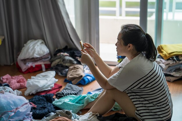 写真 服をたたみながら携帯電話を使う疲れたアジア人の主婦