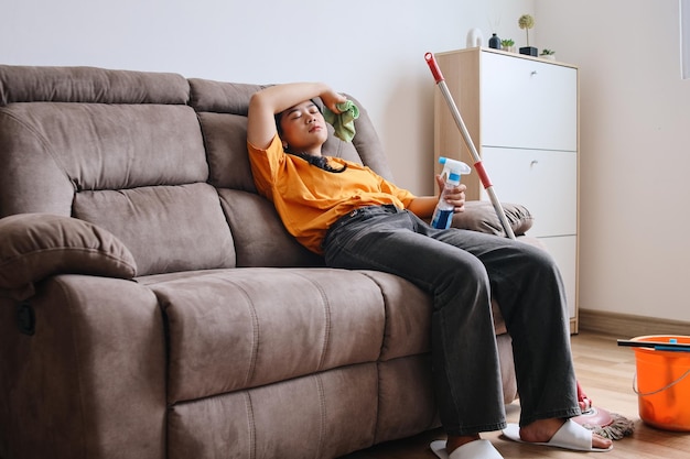 Tired Asian woman sitting on couch after cleaning the house