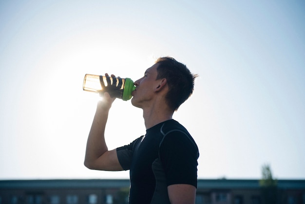 Tired athlete man drinking water from a shaker