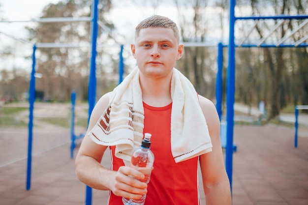 Tired athlete recharging with water bottle after training sporting guy with his water bottle taking