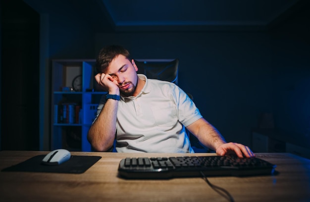 Tired bearded man lies in a chair at work at home at the computer and sleeps while working