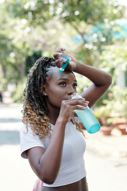 Giovane sportiva nera stanca che beve acqua dolce dopo l'allenamento all'aperto