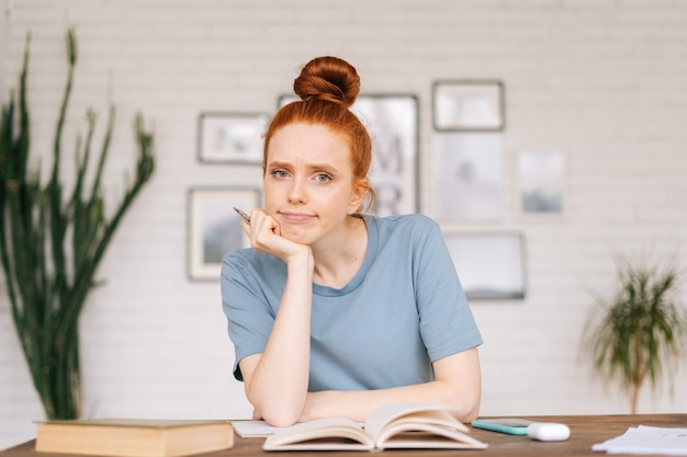 Photo tired bored girl student sitting at a table with textbooks and a workbook looking at camera