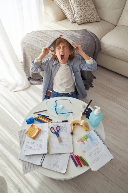 Tired boy covering head with copybook and shouting