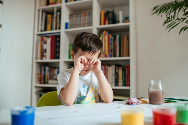 家のテーブルに座っている疲れた少年