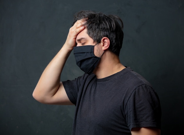 Tired brunet man in in black facemask on dark wall