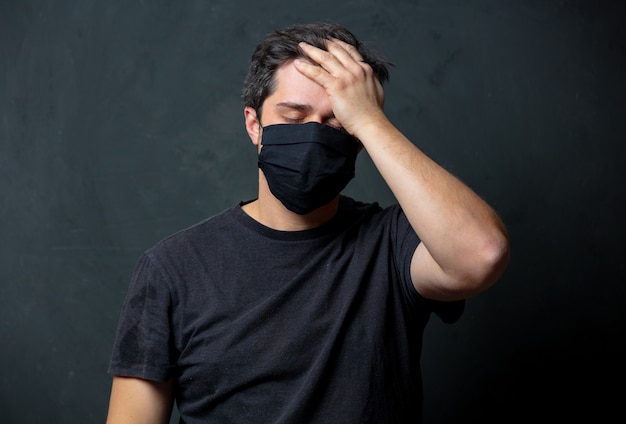 Tired brunet man in in black facemask on dark wall