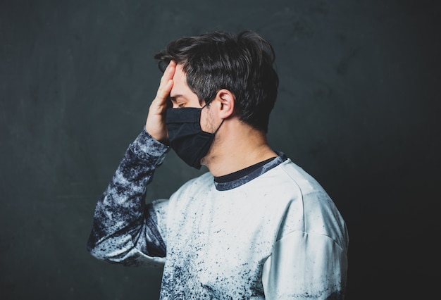 Tired brunet man in in black facemask on dark wall