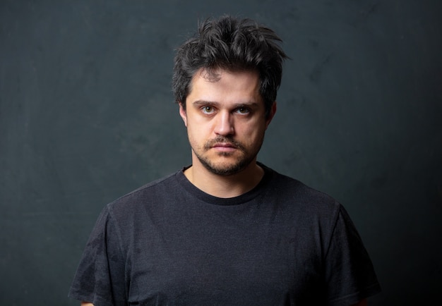 Photo tired brunet man in black t-shirt on dark wall