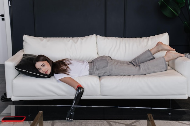 Tired brunette girl with hand prosthesis relaxing on couch Rehabilitation for people after trauma