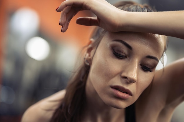 Photo tired brunette wiping sweat in the gym