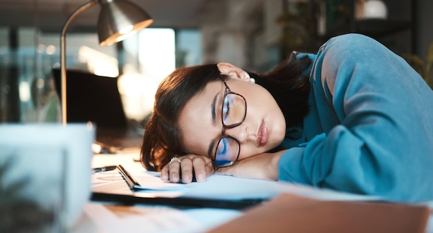 Burnout stanco e sonno con una donna d'affari che dorme sulla scrivania mentre lavora su un computer alla scrivania del suo ufficio problema di salute mentale o esausto con una giovane impiegata al lavoro di notte