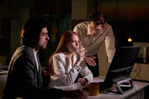 Tired Business People Using Desktop Computer, At Night, Discussing Explaining Specific Tasks, Account Handling and Strategic Moves. People Late at Night in Big Corporate Office