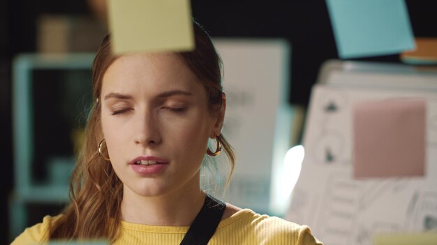 Photo tired business woman grabbing head near stickers board in modern office