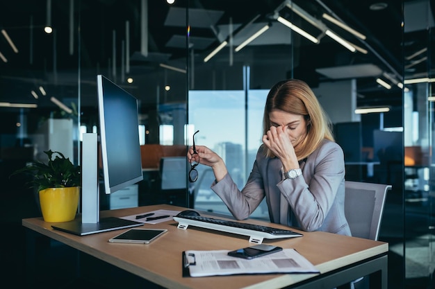 現代のオフィスの目の痛みでコンピューターに取り組んでいる疲れたビジネス女性