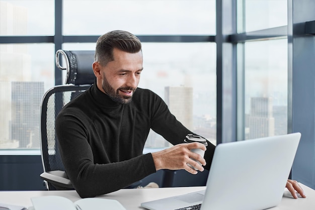 Tired businessman drinks coffee sitting at his desk