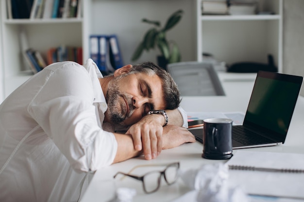 疲れたビジネスマンがofficexAでドキュメントとラップトップを使って仕事中に眠りに落ちる