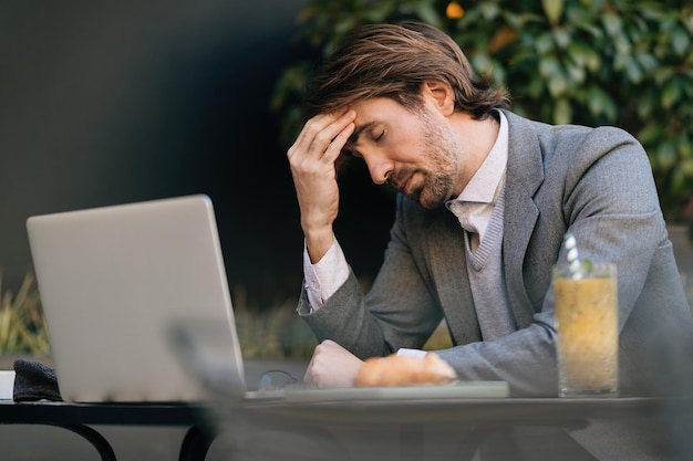 Tired businessman having a headache while sitting with eyes
closed in outdoor cafe