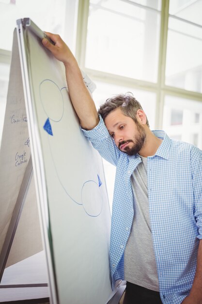 Tired businessman leaning on whiteboard in office