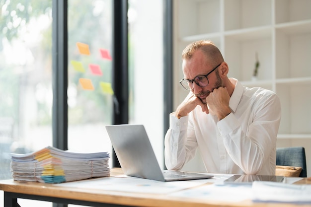 Tired businessman looking at laptop while sitting at desk in office