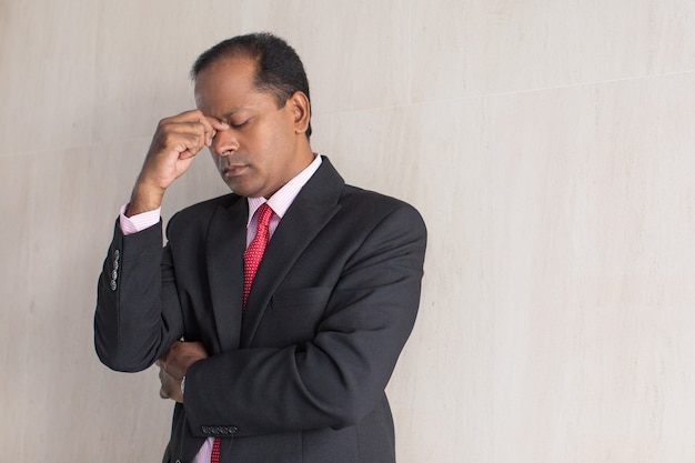 Tired businessman rubbing eyes standing at wall