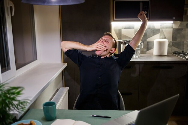 Tired businessman sitting at the table at home, modern cozy house, looking at the laptop screen, feels pleased with pride for the work done, calm person is resting, hands resting behind his head